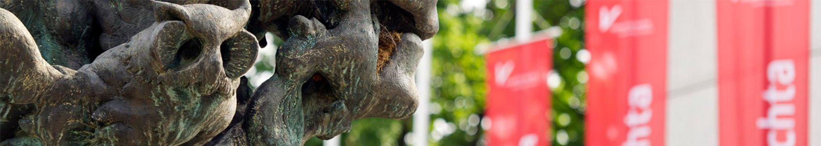 Nahaufnahme von der Skulptur vor dem Universitätshaupteingang. Im Hintergrund Rote Uni Vechta Flaggen.