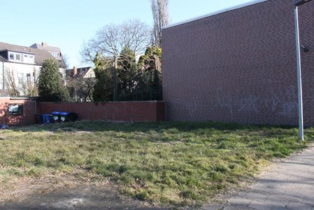 Ehemalige Brachfläche am Rathausweg in Cloppenburg. Kurzer Rasen, dahinter eine Hausfassade und im Hintergrund Müllcontainer.