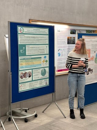 Die Vortragende Projektmitarbeiterin Lena Neumann vor dem Poster.