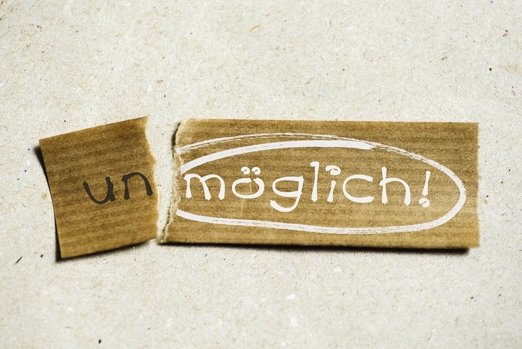 Ein alter und zerissener Zettel, links die Silbe "un" in schwarz, rechts das Wort "möglich!" in weiß und eingekreist.