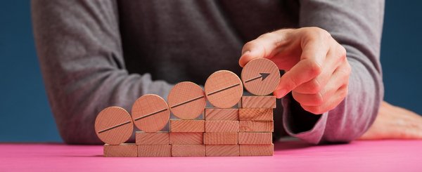 Man making a stairway like structure of wooden pegs and circles with an arrow pointing upwards in a conceptual image of personal vision and aspirations.