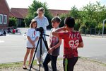 Drei Kinder arbeiten als Team mit einer Fotokamera und werden von einer Studentin beaufsichtigt