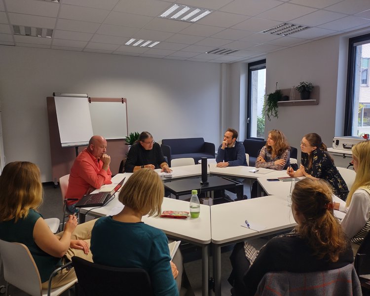 Eine Gruppe bei einem Workshop sitzt an einem runden Tisch zusammen.