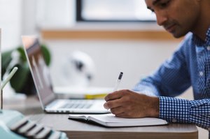 Mann schreibt Notizen neben Laptop Mann schreibt Notizen neben Laptop