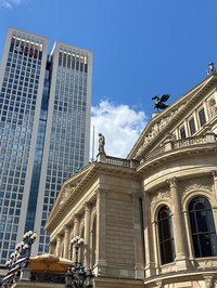 Zwei Gebäudeansichten aus Frankfurt. Rechts im Bild ein Ausschnitt der Front der Alten Oper und links, ein wenig im Hintergrund, ein für Frankfurt typisches modernes Hochhaus. 