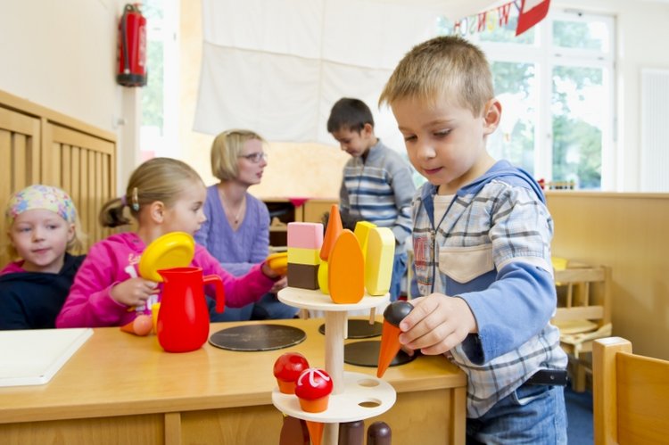 Kinder spielen, im Hintergrund passt eine Erzieherin auf.