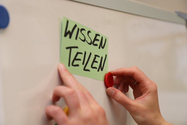 Moderationskarte Wissen teilen. Foto: Friedrich Schmidt Jemand hängt eine Moderationskarte mit der Aufschrift Wissen teilen an eine Magnetwand.