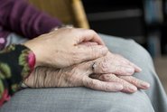 Eine Person legt ihre Hand auf die Hände einer älteren Person