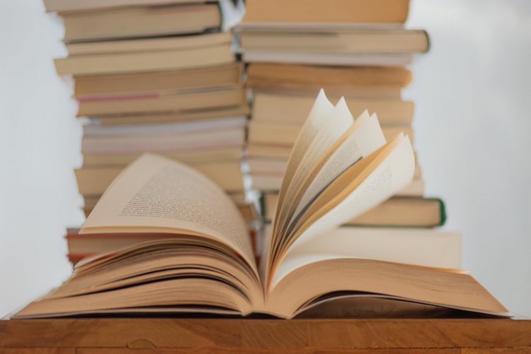 Ein Foto von einem Stapel Büchern und einem aufgeschlagenem Buch (Quelle: Unpslash)