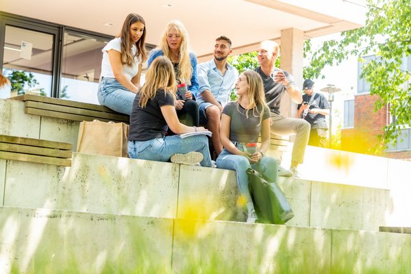 Eine Gruppe Studierender sitzt draußen in der Sonne.