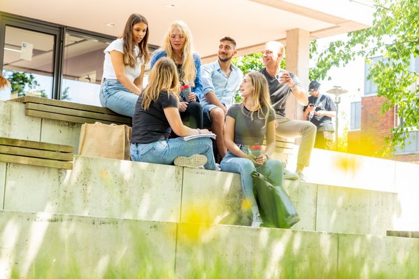 Eine Gruppe Studierender sitzt draußen in der Sonne.
