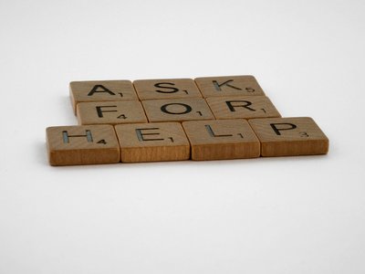Buchstaben auf Holzsteinen, die den Text ASK FOR HELP formen