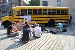 Teilnehmende sitzen vor dem MO•KU•LAB Bus auf einem Podest und arbeiten