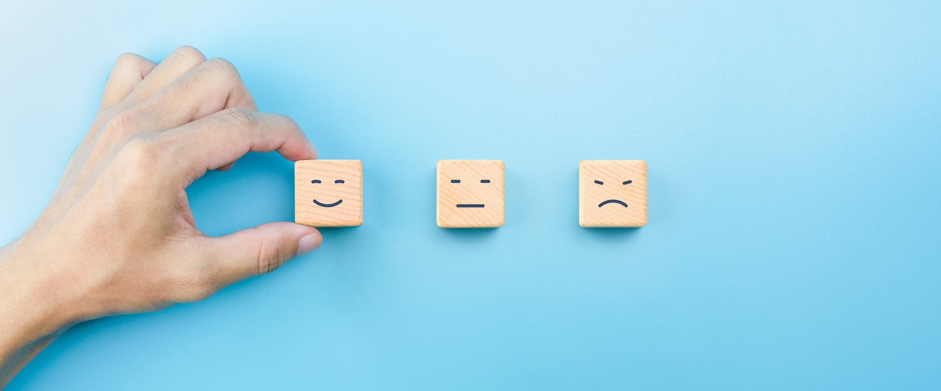 Customer service evaluation and satisfaction survey concepts. The client's hand picked the happy face smile face icon on wooden cubes on blue background