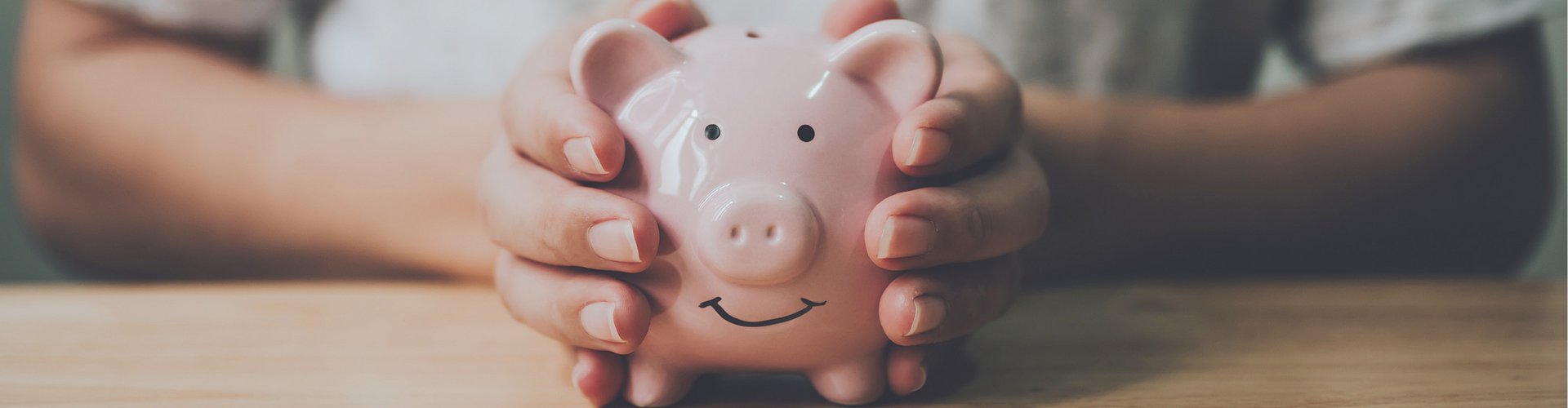Zwei Hände halten ein rosanes Sparschwein, welches lächelt
