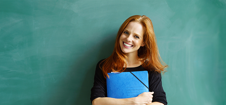 Lächelnde Lehrerin vor Tafel mit Mappe in der Hand