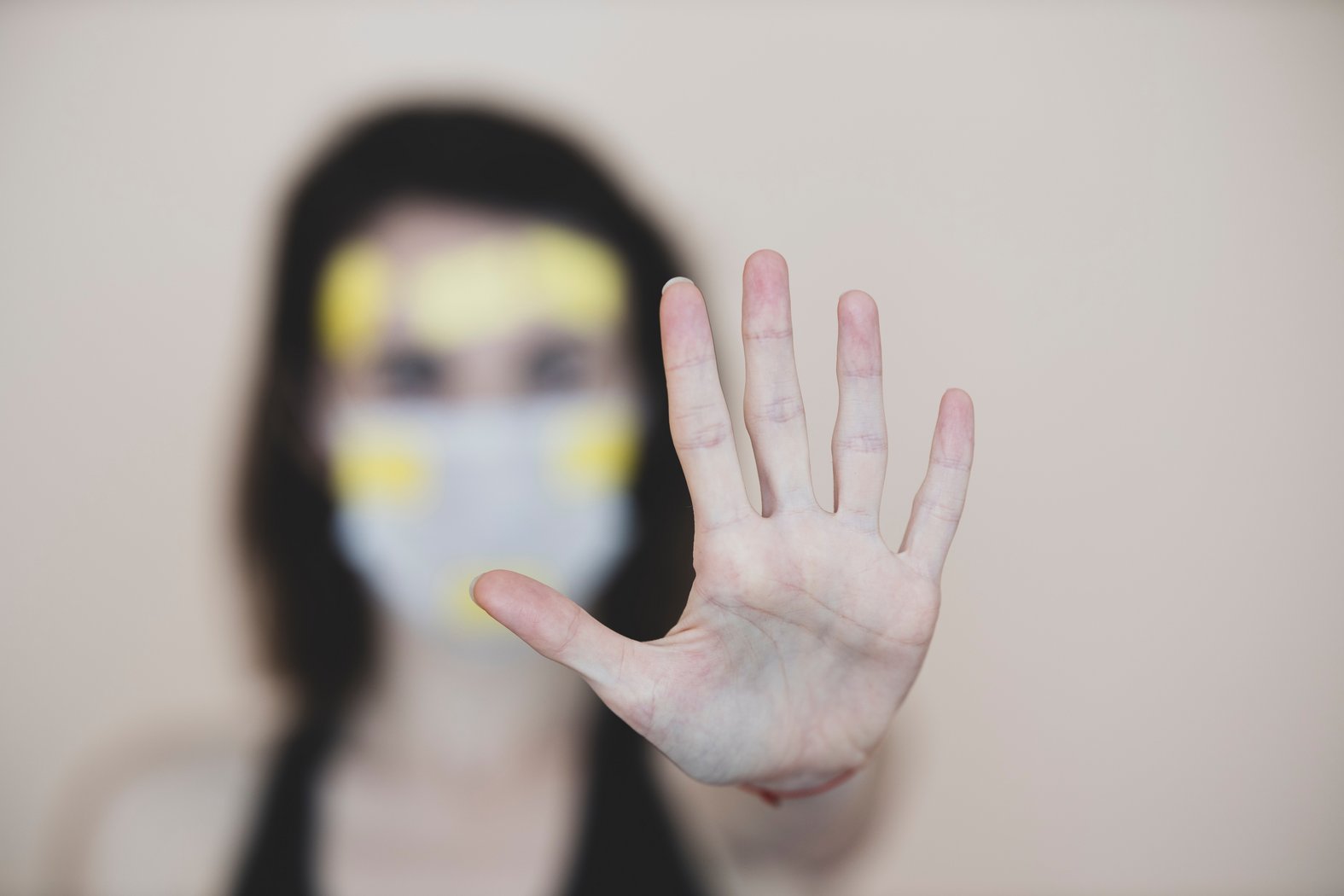 Person mit Maske, die den linken Arm und die linke Hand der Kamera entgegenstreckt (nonverbales Stop-Zeichen)
