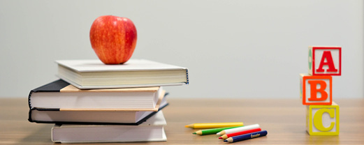 Tisch auf dem Bücher mit einem Apfel, Stiften und ABC Würfeln liegen.