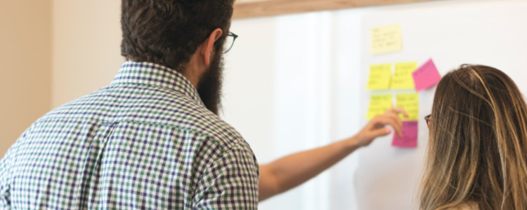 Lehramtskolleg*innen stehen zusammen und kleben Post-Its an eine Tafel.