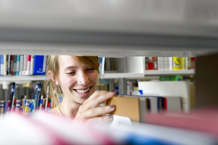 Frau entnimmt ein Buch aus dem Regal der Bibliothek