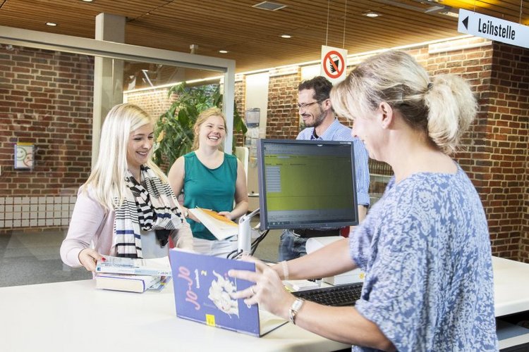 Vier Personen sind in der Bibliothek am Schalter zu sehen